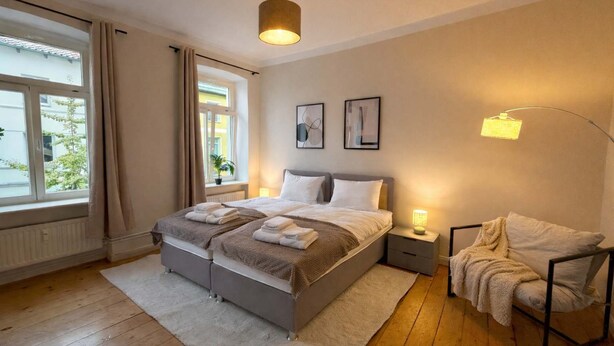 A bedroom with a large bed, bedside tables, a floor lamp, and a window with curtains. - Dora - Charming apartment in the heart of Schwerin (Schwerin)