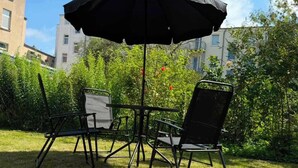 An outdoor patio with a table and chairs, an umbrella, and a view of buildings and greenery. - Dora - Charming apartment in the heart of Schwerin (Schwerin)