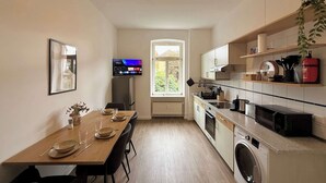 A compact kitchen with a dining area, a washing machine, and a TV mounted on the wall. - Dora - Charming apartment in the heart of Schwerin (Schwerin)