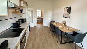 A modern kitchen with a built-in stove, microwave, and sink. There is a dining area with a table set for four and a bed in the background. - Dora - Charming apartment in the heart of Schwerin (Schwerin)