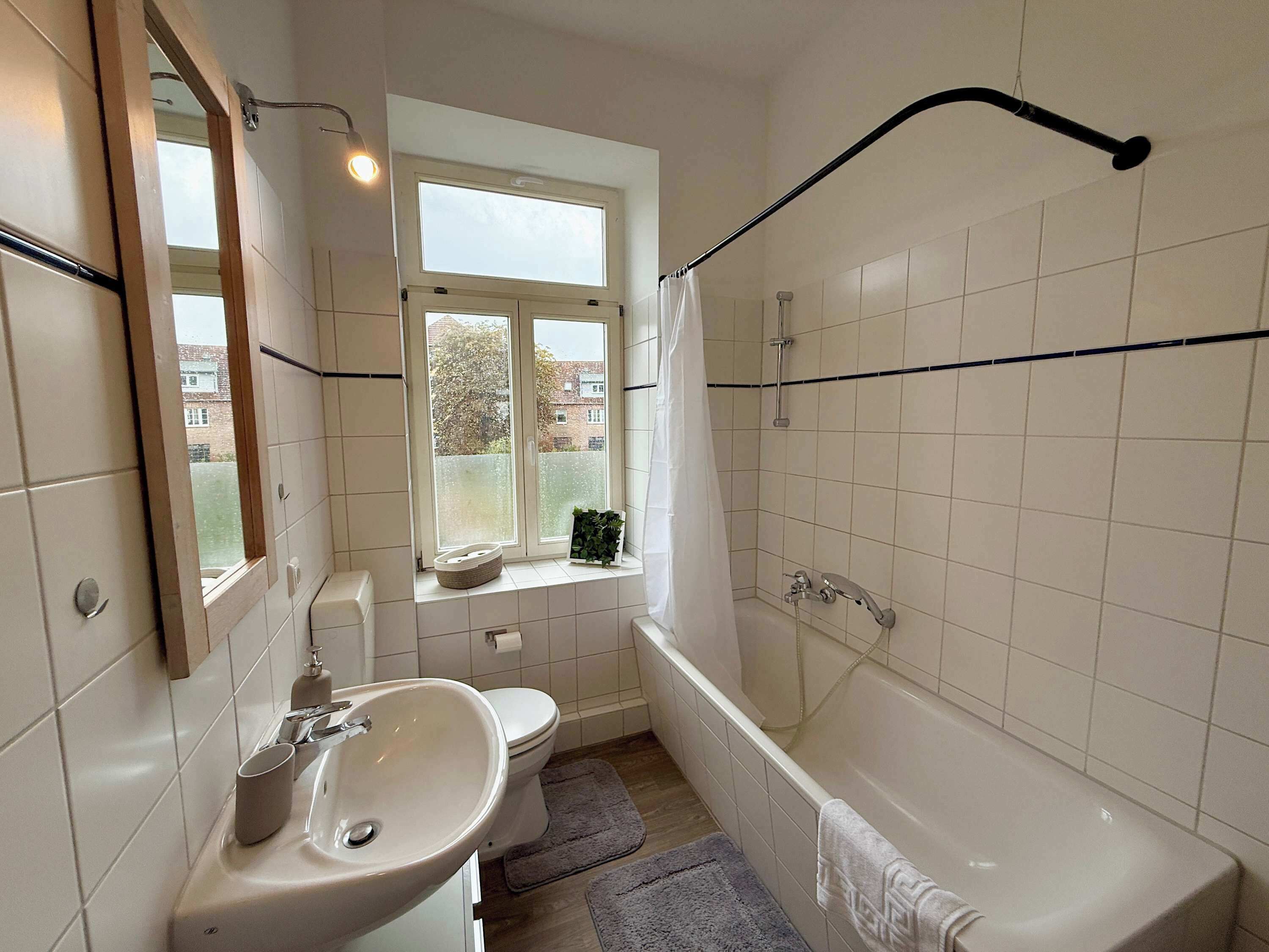 A bathroom with a white sink, toilet, and bathtub. There is a window with a view of buildings outside.