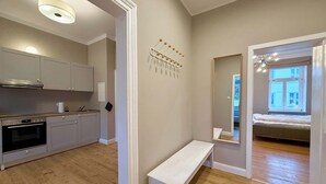 Eine moderne Küche mit weißen Schränken, einem eingebauten Backofen und einer Holz Arbeitsplatte. In der Mitte des Raumes befindet sich eine weiße Sitzbank, und im Hintergrund ist ein Bett durch einen offenen Durchgang sichtbar.