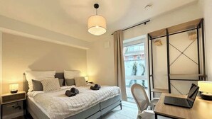 Ein modernes Schlafzimmer mit Bett, Nachttischen, einem Schreibtisch mit Laptop und einem großen Fenster mit Blick.