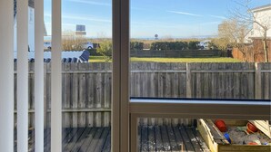 Vista attraverso una finestra su un cortile con recinzione in legno, un prato e cielo sereno.