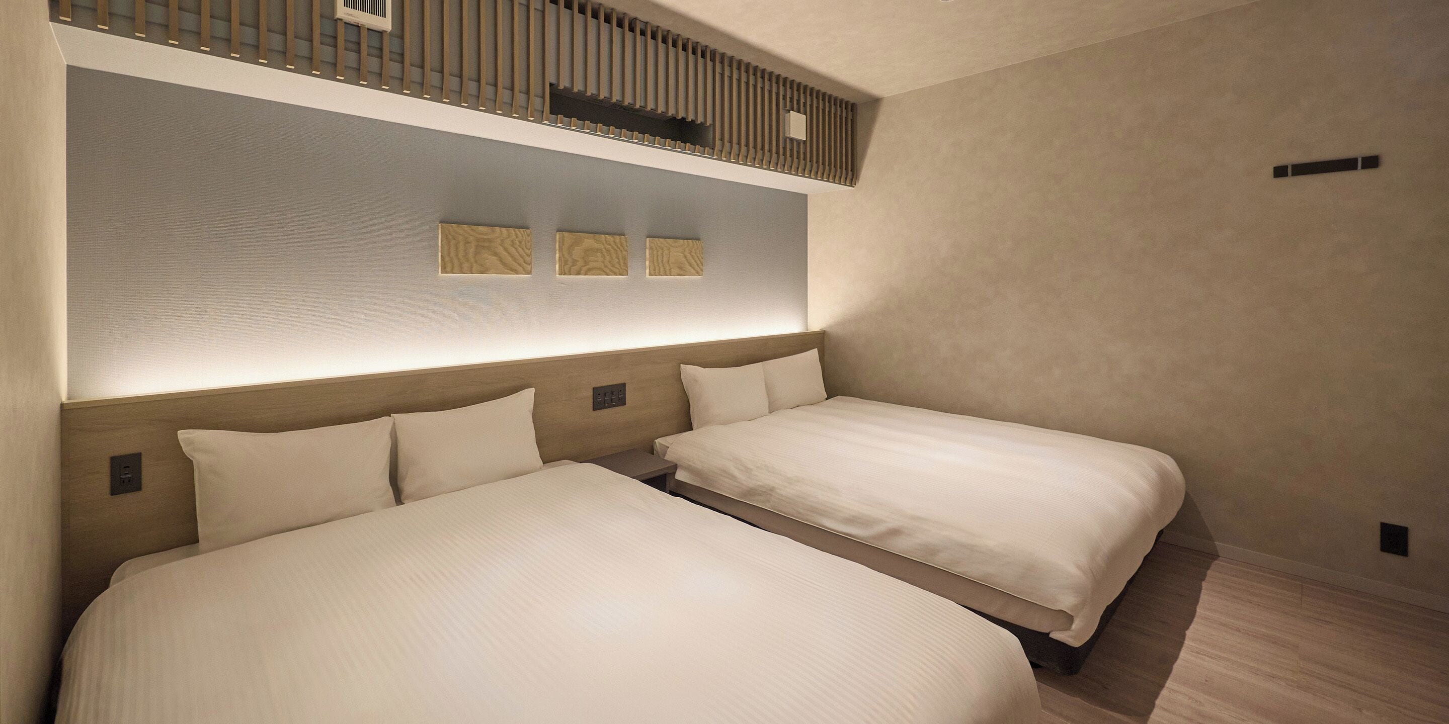 A hotel room with two beds, a wooden headboard, a wall-mounted light fixture, and a small shelf with decorative items.