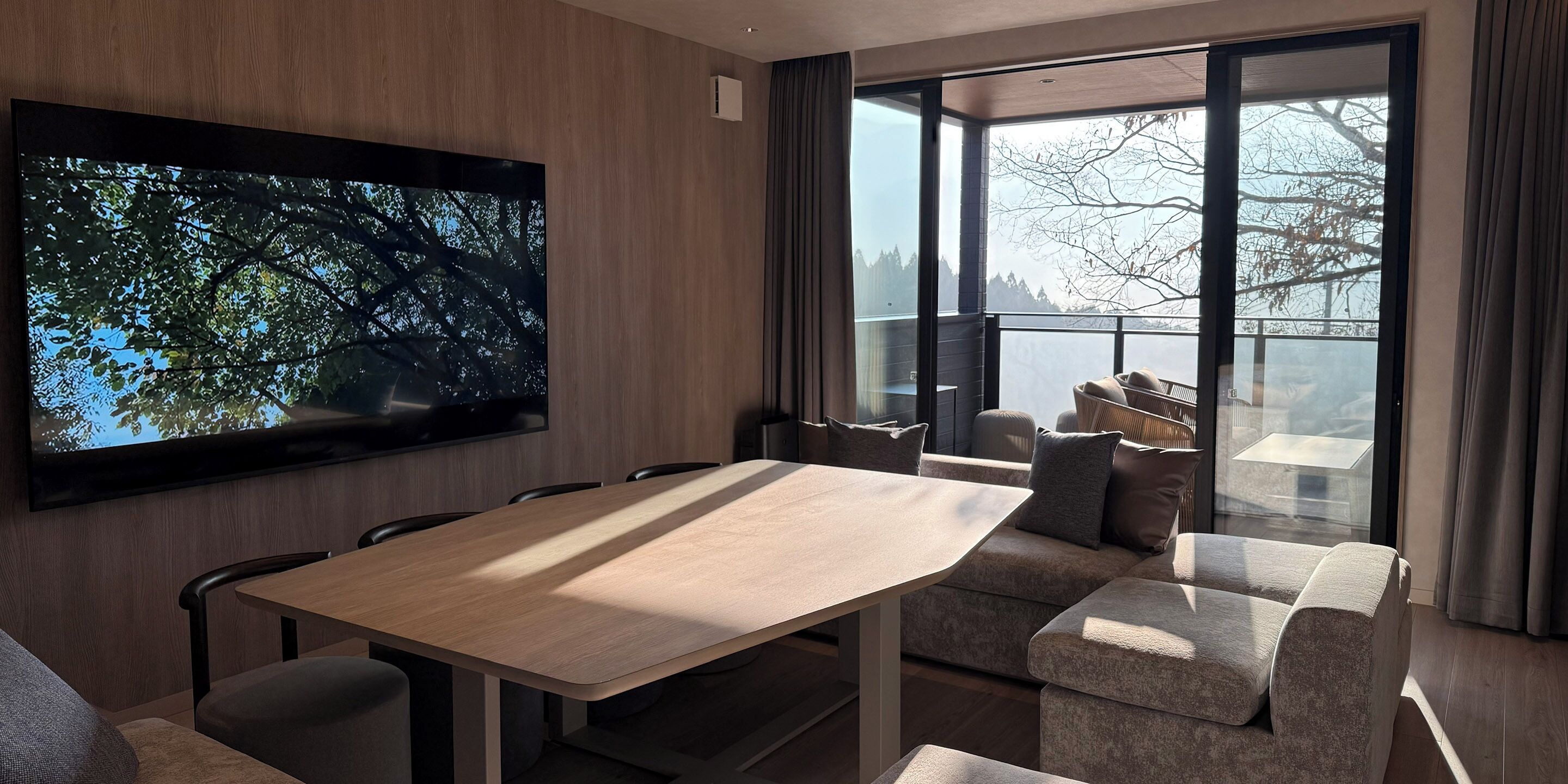 Una sala de estar moderna con un televisor de pantalla plana grande montado en la pared, una mesa de comedor de madera y un espacio de estar cómodo con sofás y sillones.