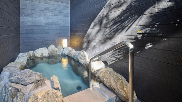 A hot spring area with a stone pool surrounded by rocks, a metal handrail, and a wooden wall. - Rakuten STAY VILLA Yufuin Onsen (Yufu)