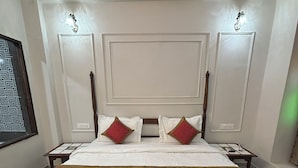 A large bed with a wooden frame, white bedding, and red pillows. There are two bedside tables with lamps. The room has a patterned carpet and a decorative ceiling. - Hotel Royale Plazo (Jodhpur)