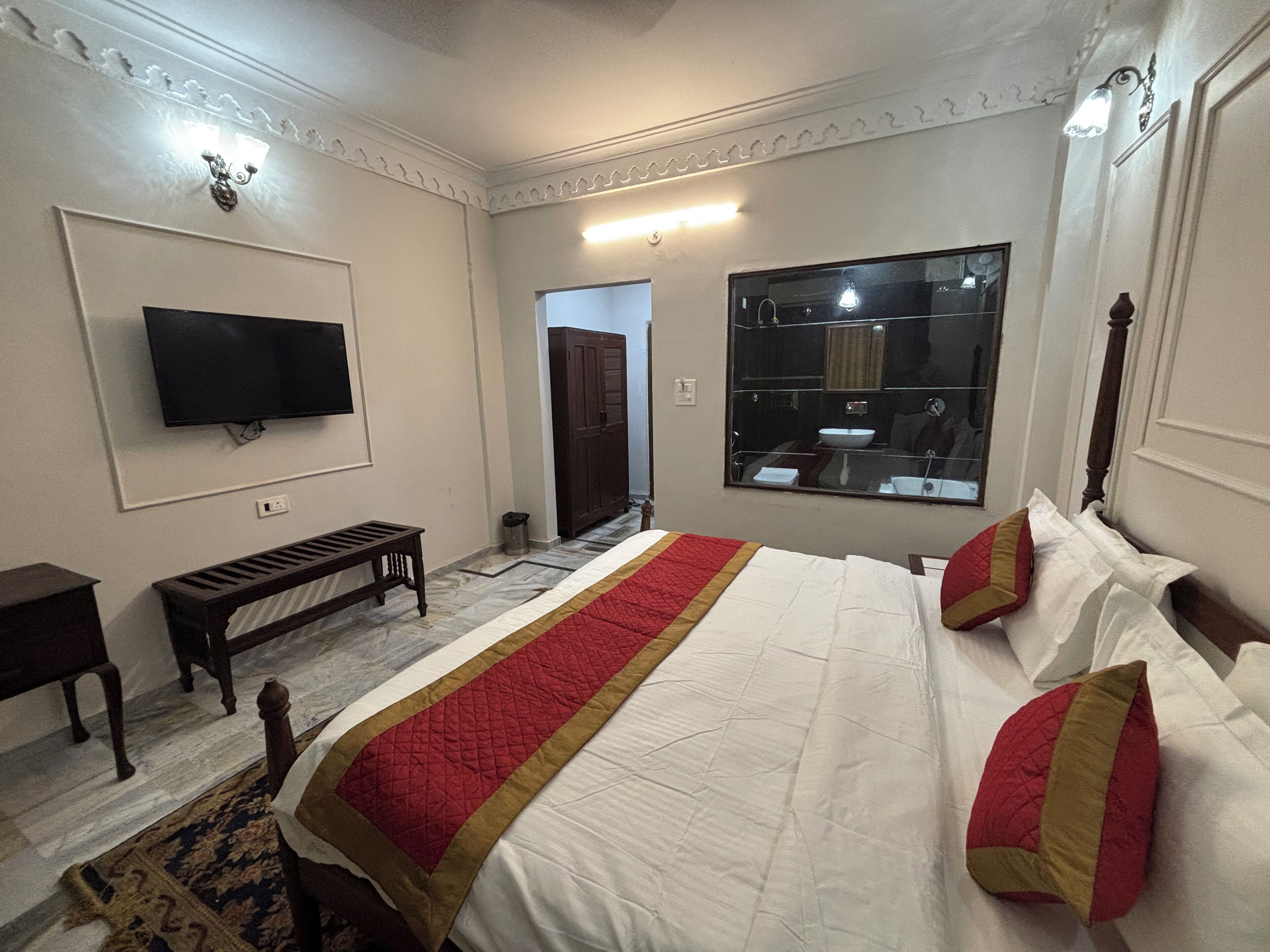 A hotel room with a large bed, a television, a mirror, and a wardrobe.