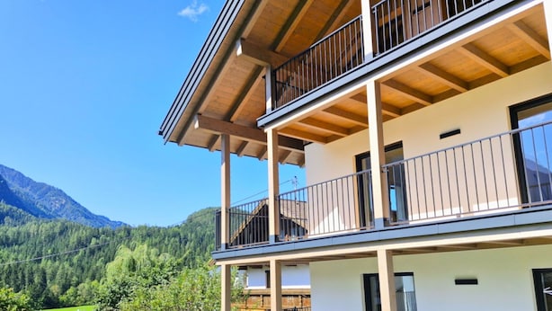 Un immeuble à plusieurs étages doté de balcons, avec une vue sur les montagnes et un jardin bien entretenu.