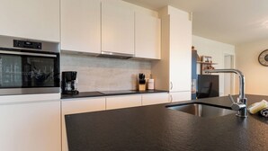 A modern kitchen with white cabinets, a black countertop, stainless steel sink, and an AEG oven. - Cosy apartment for 6 people with A/C, WIFI, TV and balcony (Bruges)