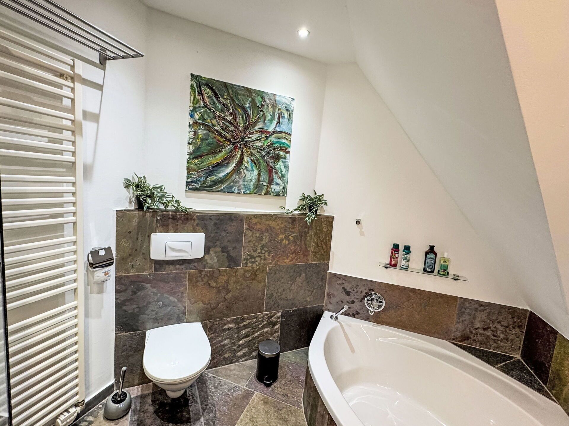 Un baño moderno con inodoro, bañera y un cuadro abstracto de gran tamaño en la pared.