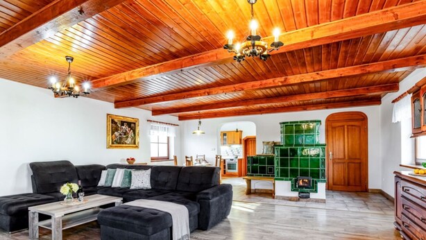 A spacious living room with a wooden ceiling, a black sofa set, a coffee table, and a green tiled fireplace. - Beautiful private villa for 10 people with WIFI, private pool, terrace and pets allowed (Lesní Chalupy)