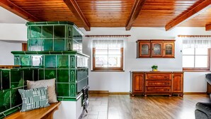 A spacious living room with a wooden ceiling, a green tiled fireplace, a wooden bench, and a wooden cabinet. - Beautiful private villa for 10 people with WIFI, private pool, terrace and pets allowed (Lesní Chalupy)