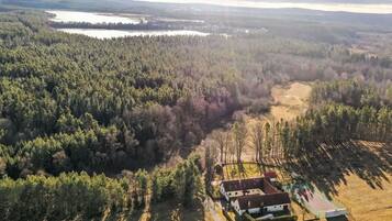 An aerial view of a property with a house, a fenced sports field, and surrounding forested area.