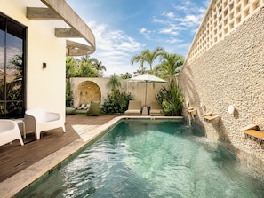 Une piscine avec une terrasse en bois, des chaises longues et un mur en pierre.