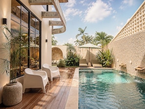 A modern outdoor pool area with a stone wall, lounge chairs, and potted plants. - Chic 4-br Villa in Central Seminyak, Beach 10 min (Seminyak)