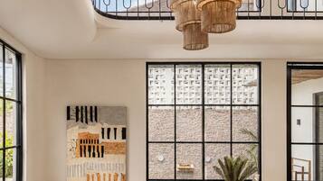 Amplia sala de estar con techo alto, un ventanal con vista a una piscina, un banco de madera y una lámpara moderna.