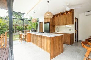 A modern kitchen with a central island, wooden cabinetry, and pendant lighting. - Exquisite 6-bedroom Retreat, Moments to Beach (Seminyak)