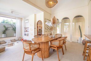 A spacious living area with a large wooden dining table surrounded by wicker chairs, a sofa, and a small side table. - 4BR Tropical Retreat With Private Pool Near Canggu (Canggu)