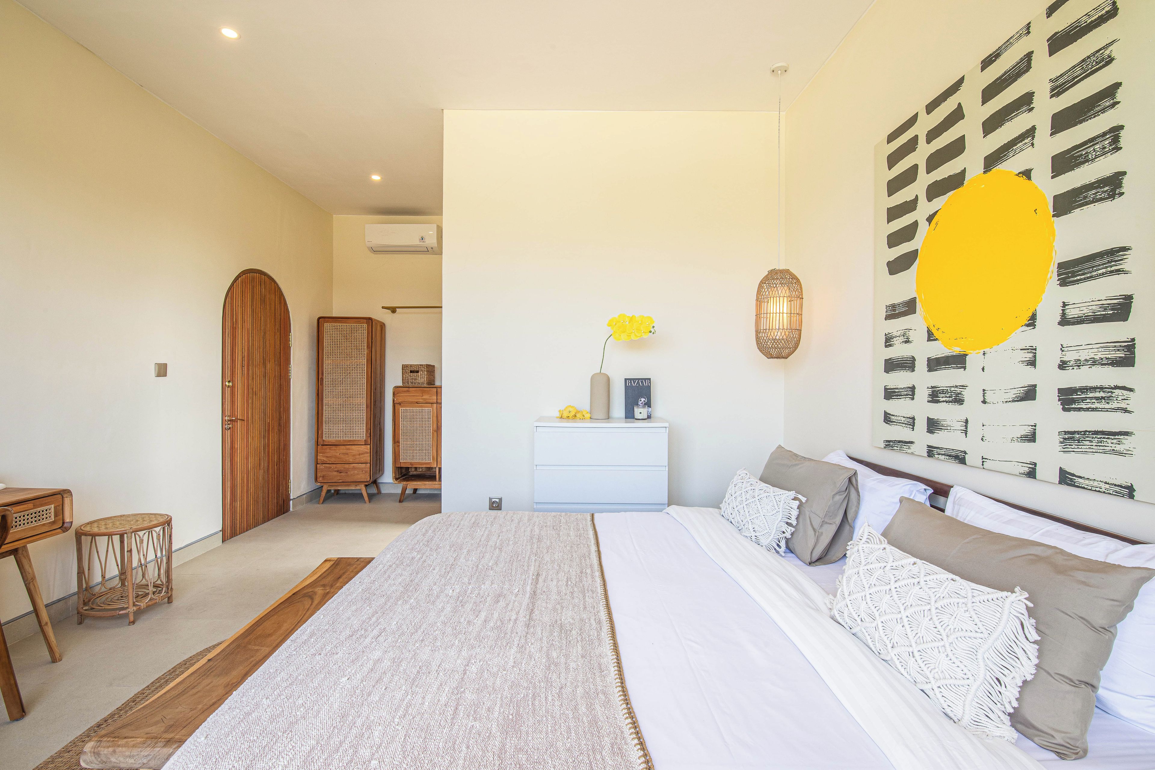 A bedroom with a large bed, bedside tables, a dresser, a wall-mounted lamp, and a decorative wall piece.