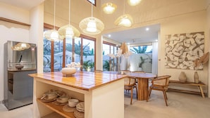 A modern kitchen with a wooden island, hanging wicker lights, and a view of the outdoors. - Chic Villa Living, Hidden Serenity of Canggu (Canggu)