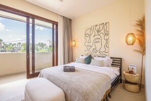 A bedroom with a large bed, a view through a sliding door, a wall-mounted artwork, and a bedside lamp. - 4BR Tropical Retreat With Private Pool Near Canggu (Canggu)