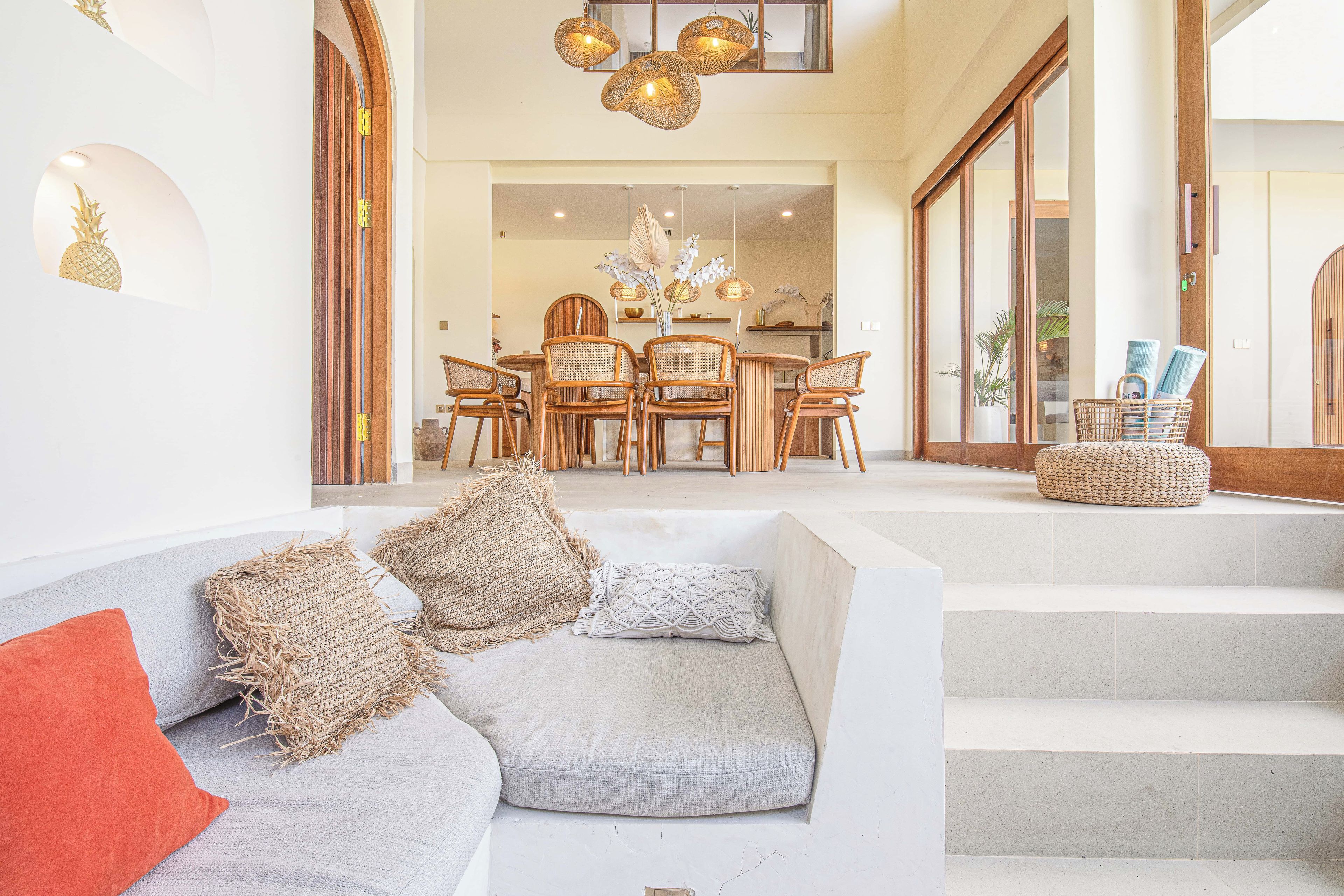 A modern living room with a grey sofa, wooden chairs, and a dining area in the background.