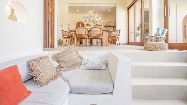 A modern living room with a grey sofa, wooden chairs, and a dining area in the background. - Chic Villa Living, Hidden Serenity of Canggu (Canggu)