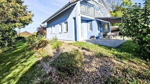 A modern two-story house with a sloped roof, a covered porch, and a landscaped garden.