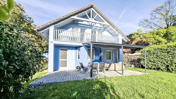 A two-story house with a balcony, a covered patio area with outdoor seating, and a well-maintained garden.