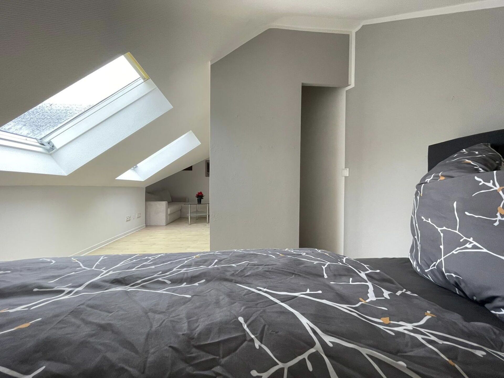 A bedroom with a skylight, a bed with a patterned bedspread, and a view into an adjacent room.