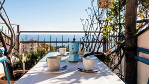 Ein Tisch für zwei mit Meerblick, eine blaue Kanne und eine Tasse auf einer Terrasse.