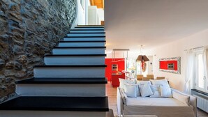 Eine Treppe mit einer Steinwand auf der einen Seite und einem modernen Innenraum mit roter Akzentwand und einer Couch auf der anderen.