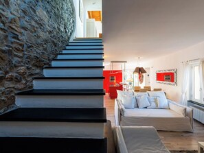 Una scala con un muro in pietra da un lato e, dall'altro, un interno moderno con una parete rossa a contrasto e un divano.