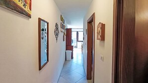 Un pasillo con suelo de baldosas, una puerta de madera y un espejo en la pared.