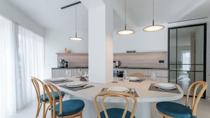 A modern dining area with a round table, four wooden chairs with blue cushions, and pendant lighting.