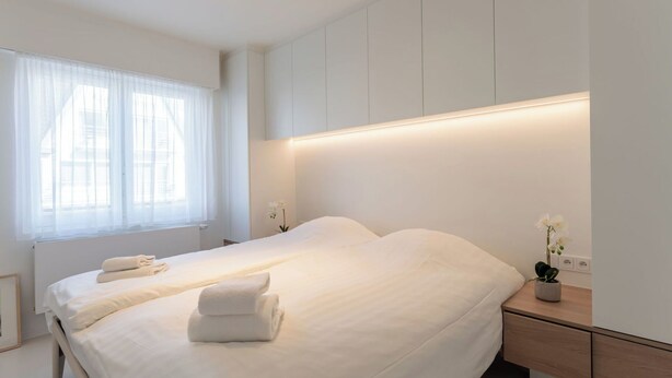 A modern bedroom with a large bed, bedside tables, and a window with sheer curtains.