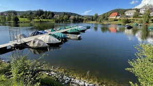 Un lac paisible, avec un quai et plusieurs tentes, entouré de maisons et de verdure.