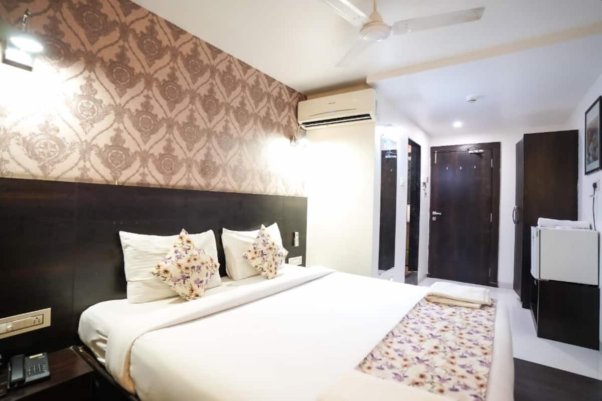 A hotel room with a large bed, a headboard, an air conditioning unit, a wardrobe, and a desk with a telephone.
