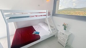 A bunk bed with a red mattress, a small bedside table with drawers, a wall-mounted light, and a window with a view of a landscape. - Stunning private villa for 5 guests with A/C, TV and balcony (Villasimius)