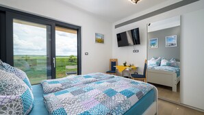 Une chambre avec une grande fenêtre, un lit avec une literie à motifs, un bureau avec une chaise et un téléviseur fixé au mur.