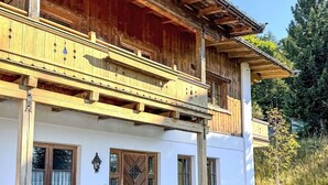 Eine zweistöckige Chalet mit Holzbalkon, Steinwand und einer Bank davor.