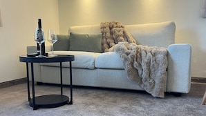 Ein Wohnzimmer mit einem beige farbenen Sofa, einem runden schwarzen Couchtisch und einem Fellteppich.