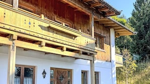 Eine zweistöckige Chalet mit Holzbalkon, Steinwand und einer Bank davor.