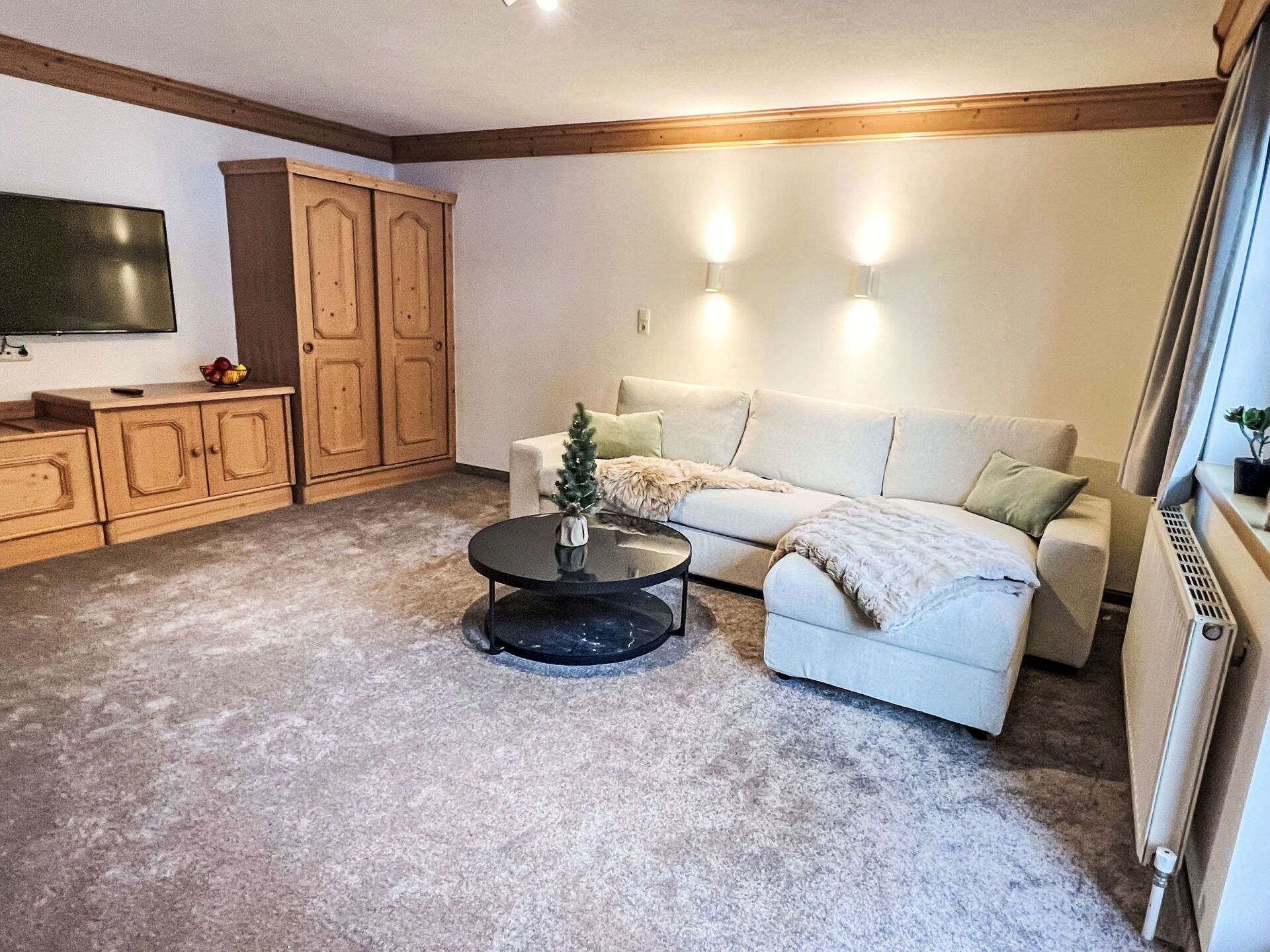 A living room with a sofa, a coffee table, a TV, wooden cabinets, and a radiator.
