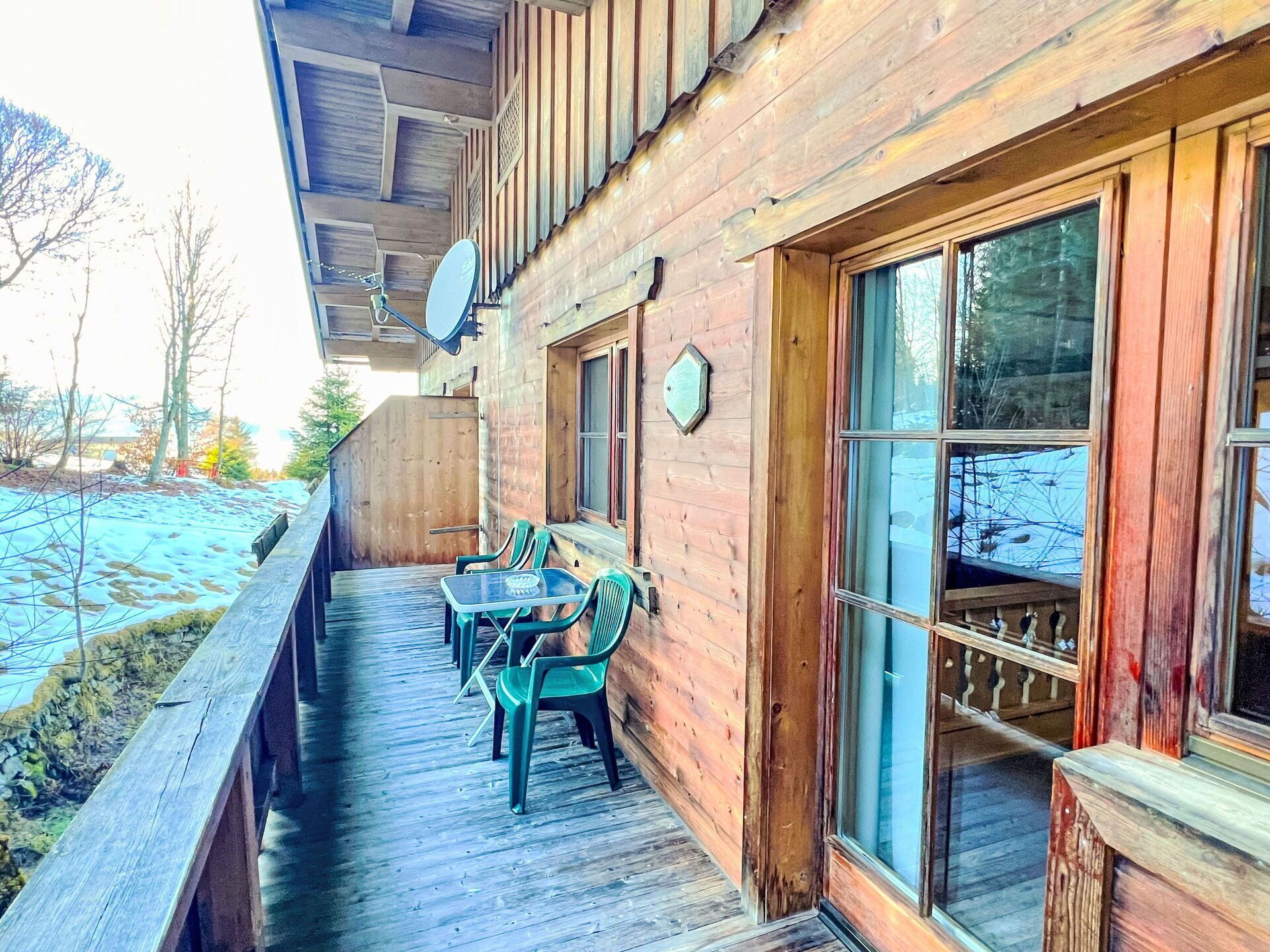 A wooden cabin with a covered porch, a dining table with chairs, and a large window.