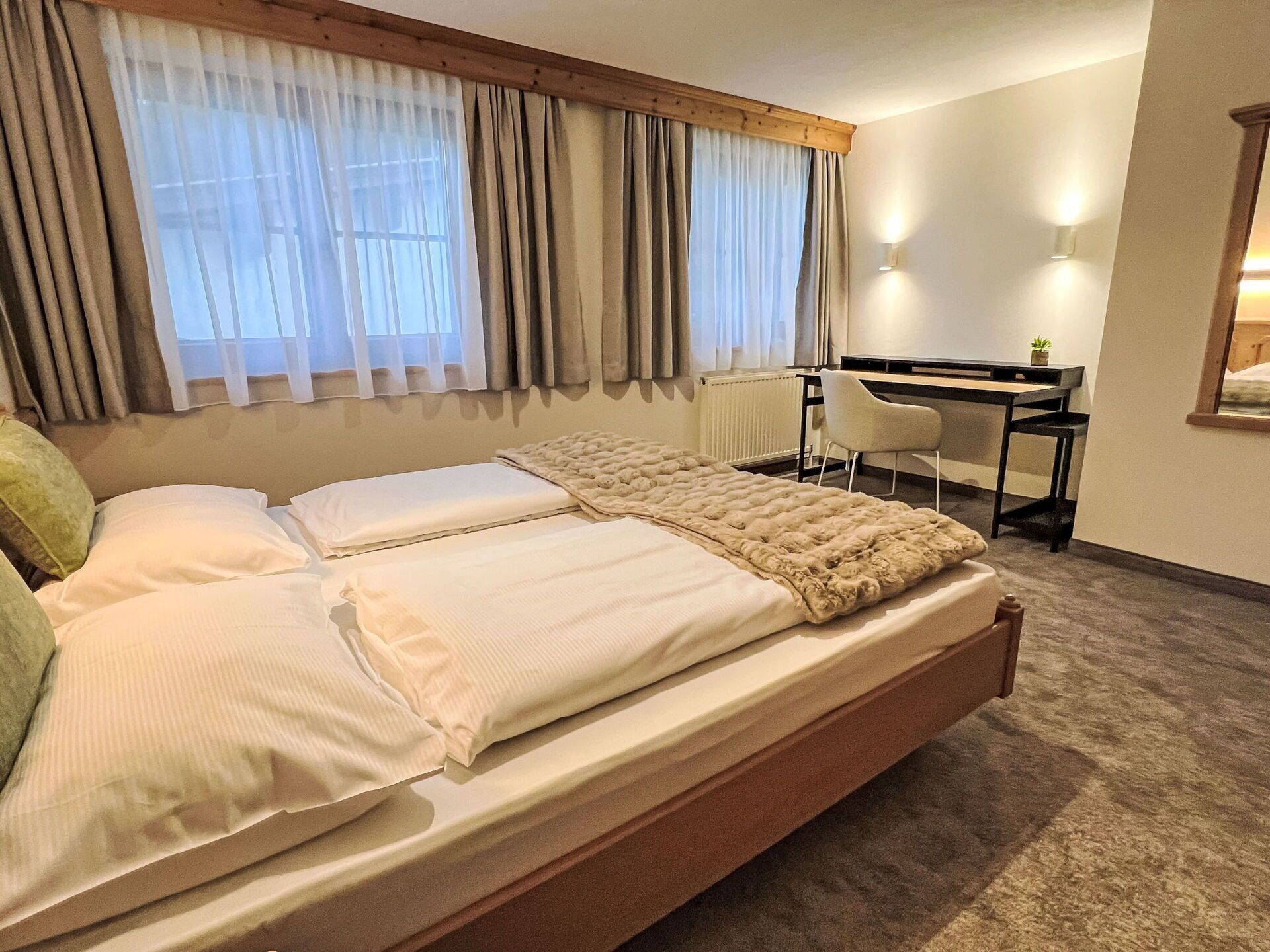 A neatly made bed with a duvet and pillows, a desk with a chair, and a radiator.