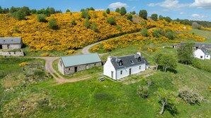 Ländliche Landschaft mit Steinhäusern, einem weißen Haus mit grauem Dach und einem mit gelben Blumen bedeckten Hügel.