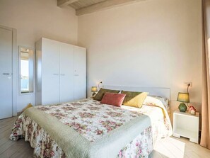 A bedroom with a large bed, a wardrobe, two bedside tables with lamps, and a window with curtains. - Lovely apartment for 4 guests with WIFI, pool, A/C, TV, balcony and pets allowed (Viddalba)